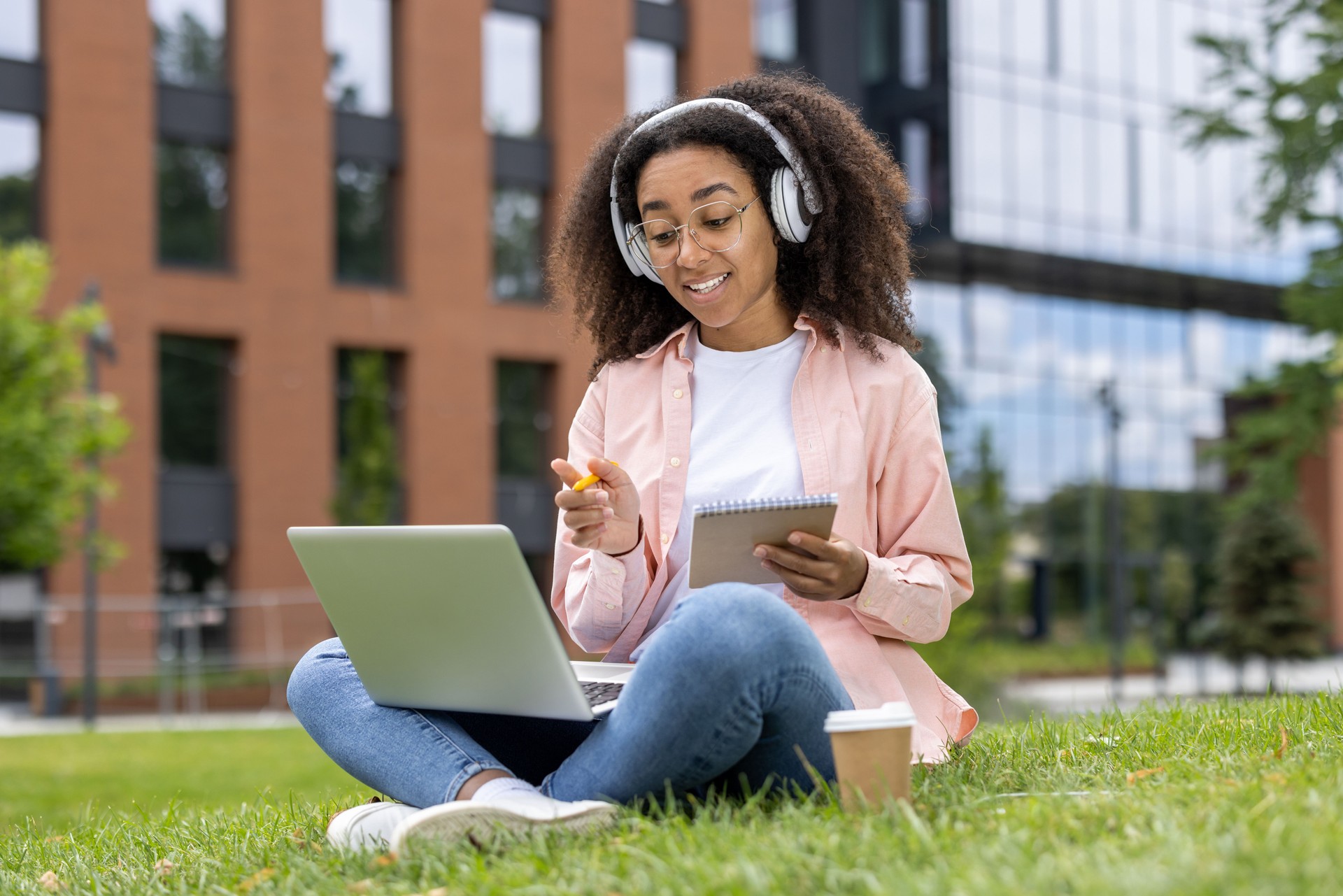 Young woman studying outdoors with laptop, headphones, and notebook at a university campus