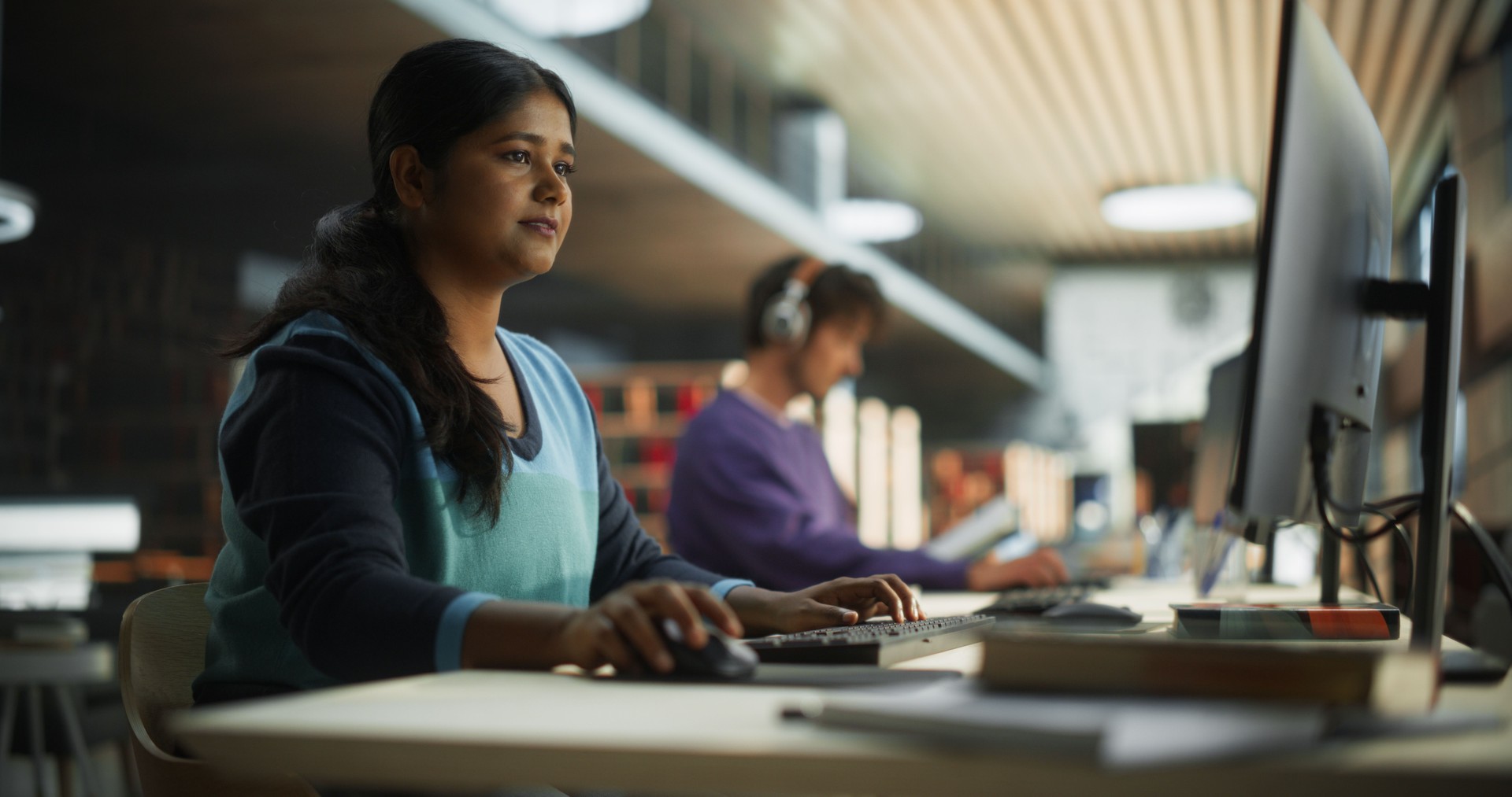 Thoughtful Indian Female Student Working on Personal Development in a Quiet Public Library with Rows of Bookshelves. Young Smart South Asian Woman Preparing for Examination in College